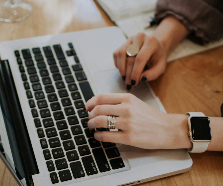 Eine Hand tippt auf einer Laptop-Tastatur, die andere hält einen Stift.