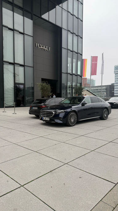 CTI Automotive Glazing Conference 2024 Schwarzes Auto auf modernem Platz vor hochglänzendem Gebäude mit Fensterfassade.