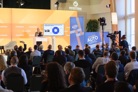 Handelsblatt Auto-Gipfel 2024 Konferenz mit einem Redner vor Publikum, Bildschirm zeigt Präsentation.