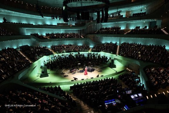 HELM AG Jubiläum 2025 Elbphilharmonie Eine Bühne in einem Konzertsaal mit grüner Beleuchtung und einem großen Publikum.