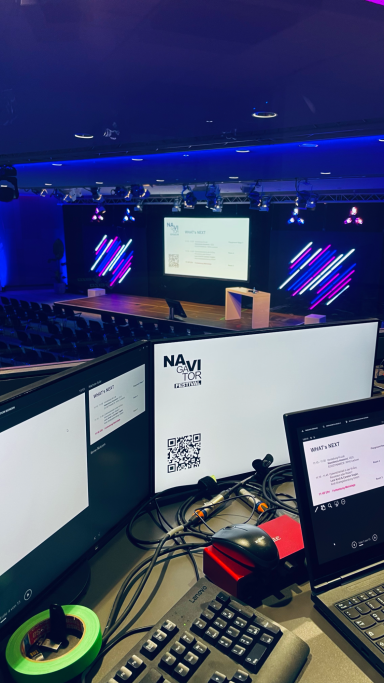 Navigator Festival 2025 Blick auf einen Konferenzraum mit Präsentationsbildschirm und technischen Geräten.