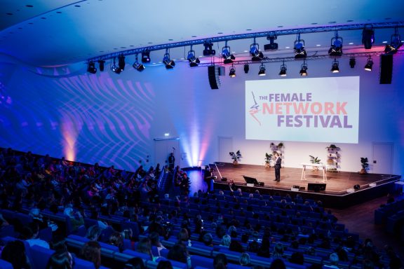 The Female Network Festival 2026 - ©Heike Katthagen Blick auf die Bühne beim Netzwerkfestival mit Publikum und Beleuchtung im Hintergrund.